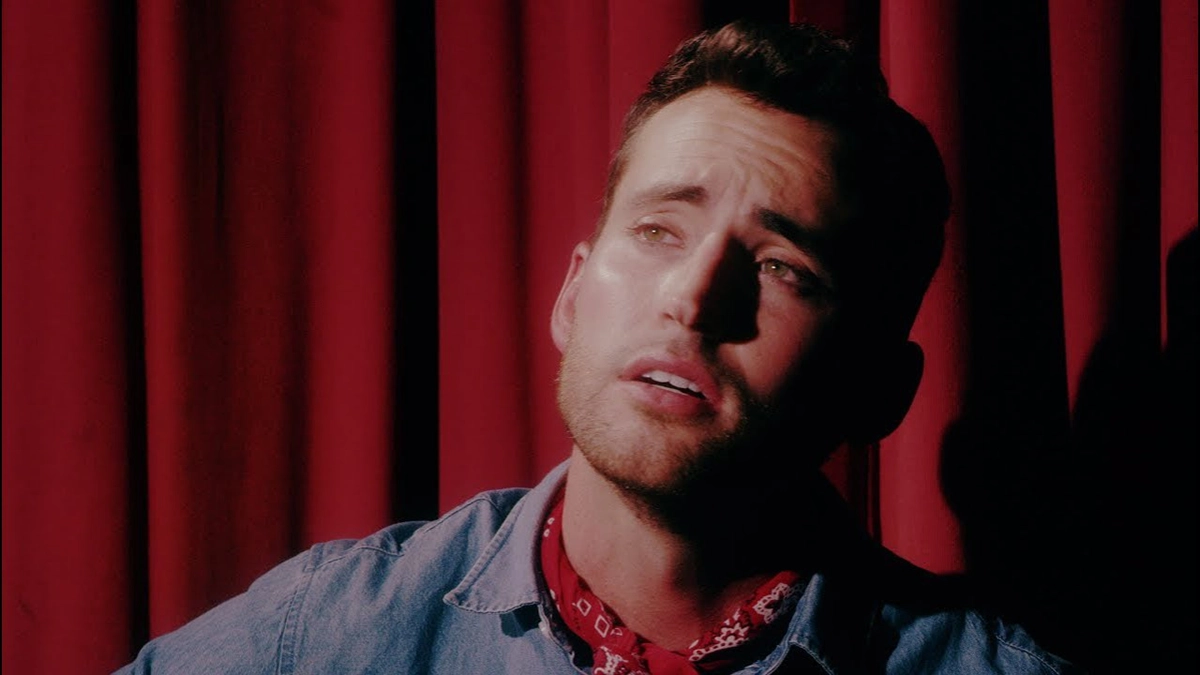 Cameron Hawthorn cowboy shirt with red and white cowboy scarf. Red stage curtin as background