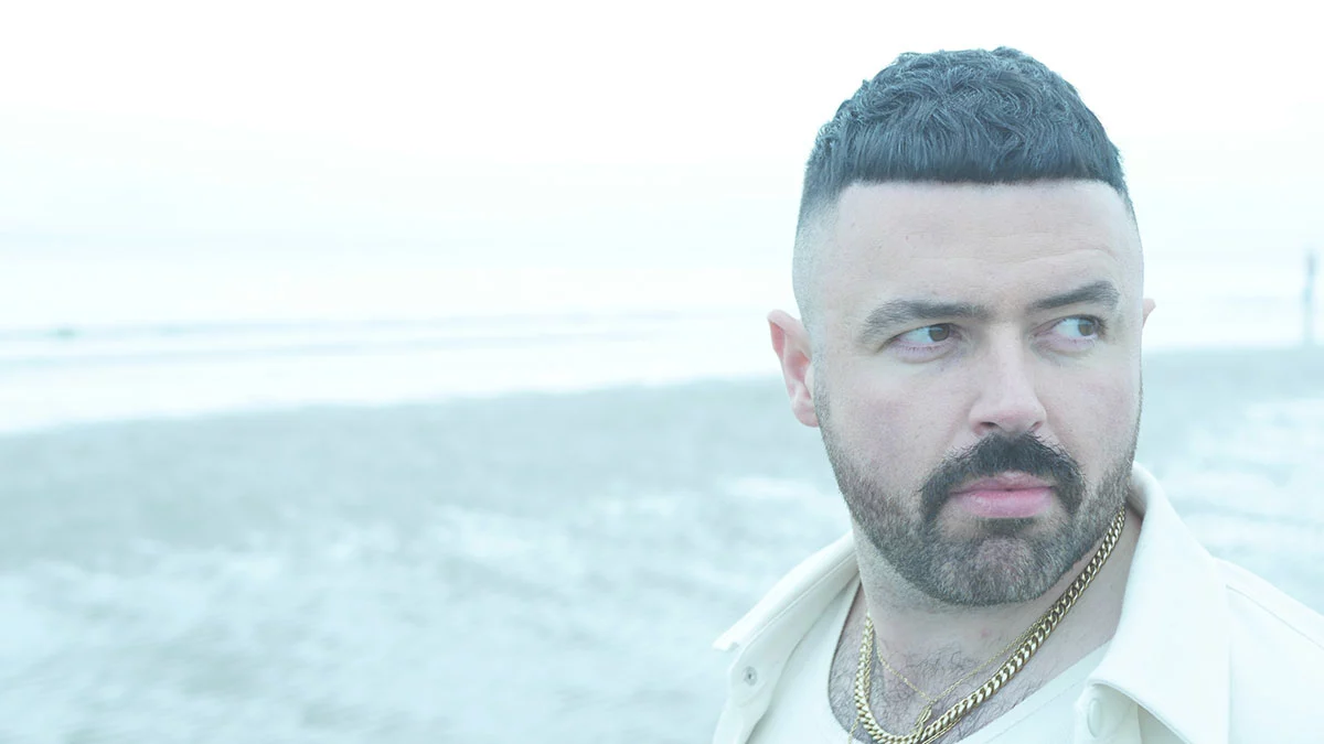 Picture of Robert O'Connor by the sea. He is in a all white suite and shirt. Dark brown hair and beard.