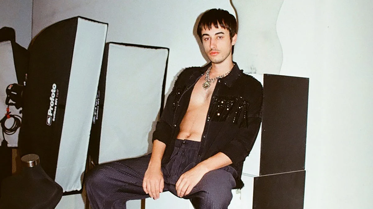 Picture of Edo Lio with black shirt half open and black trousers. Edo Lio has dark hair.