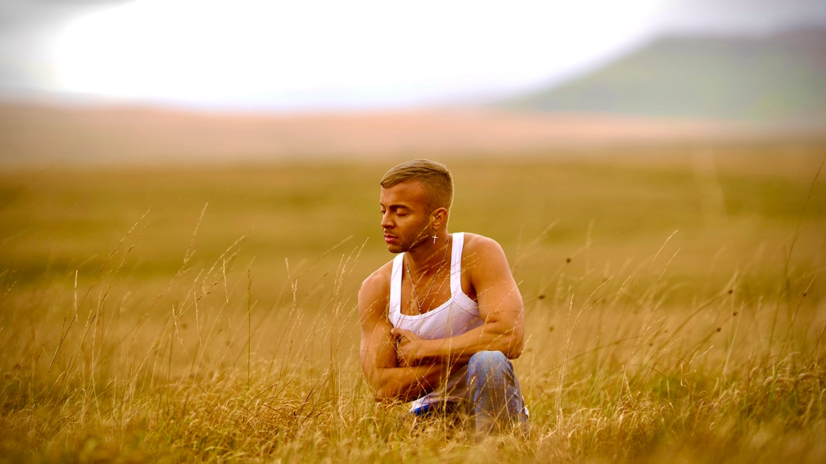 Rhian! in white tank top sitting in a meadow.