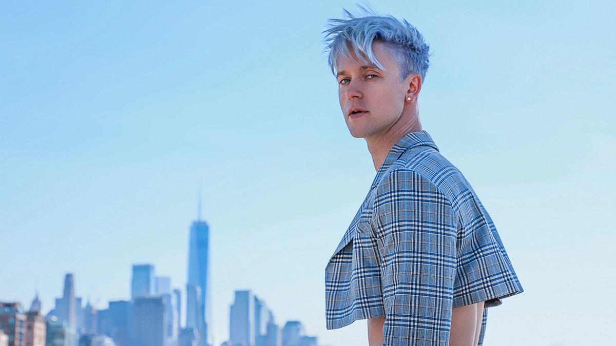 Magnus Riise with New York City in the background - He is bleached blond and has plaid (black and white) crop top jacket.