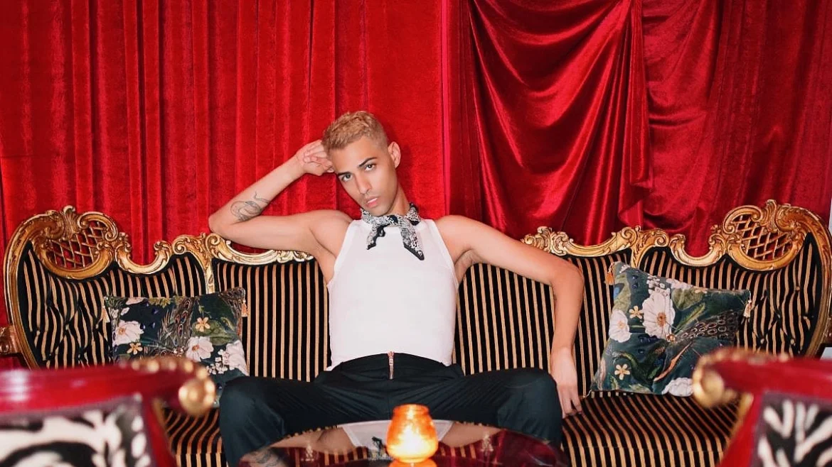 Jxckson sitting in striped coach in white tank top and black jeans - background is red