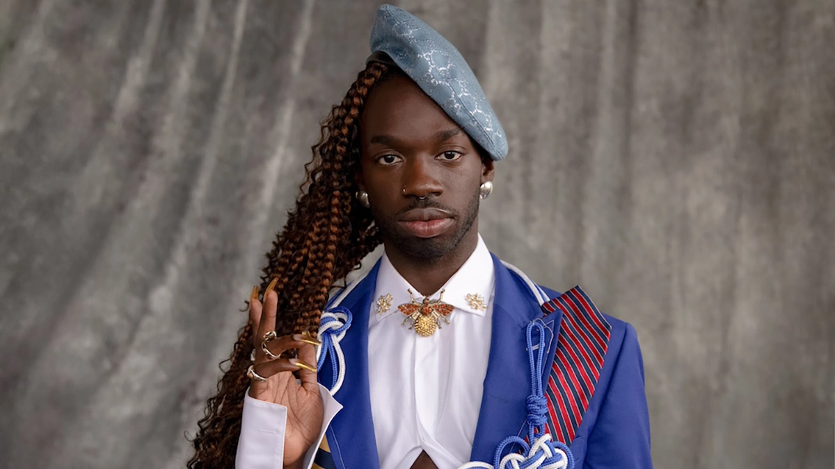 Saint Ahmad light blue-grey beret with long black curly hair. White crop top and dark blue jacket !