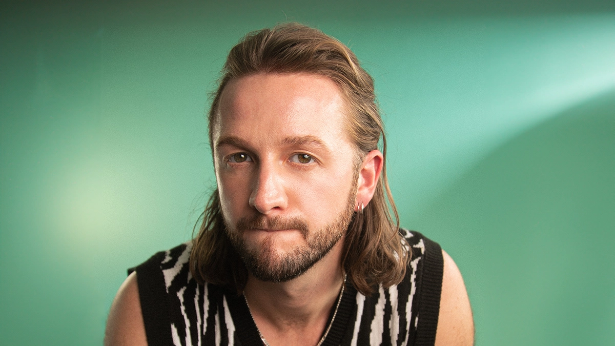 Beljune sitting with green background - having a black and grey vest leaning forward.