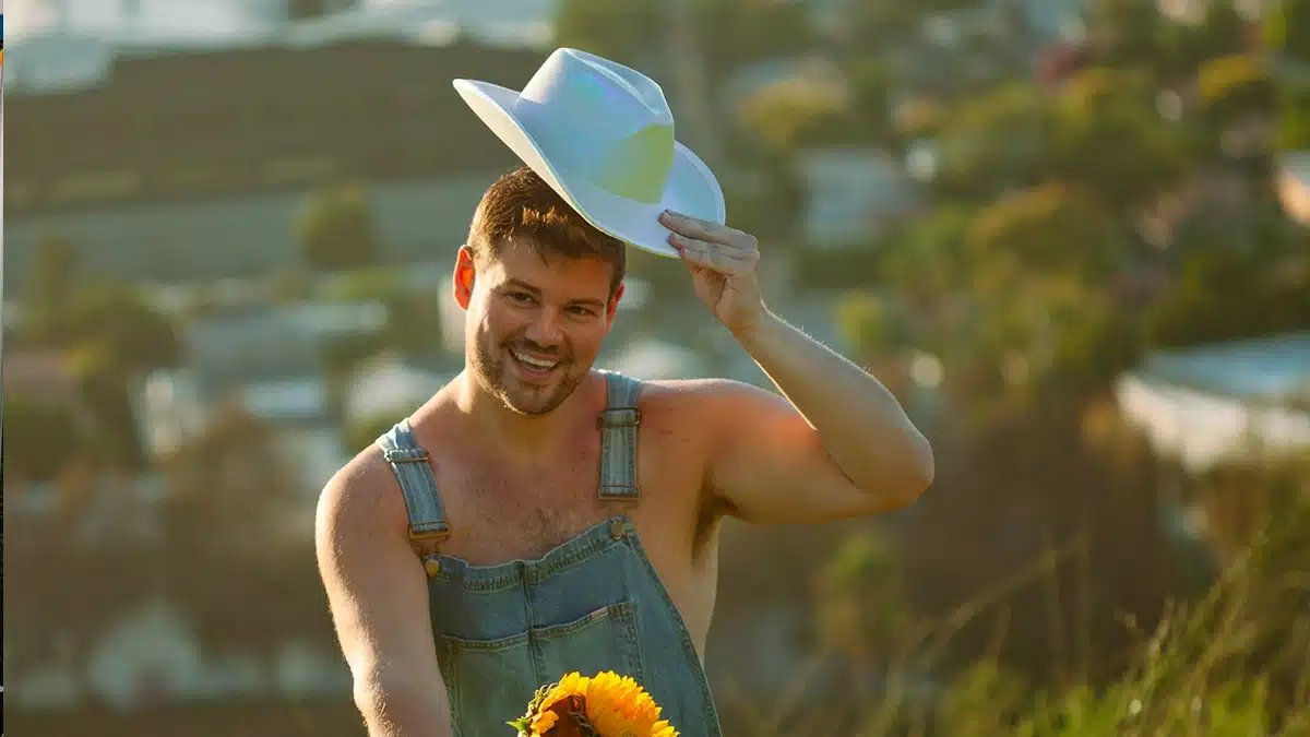 Allen Miller in Suspender trousers with no shirt an a white cowboy hat