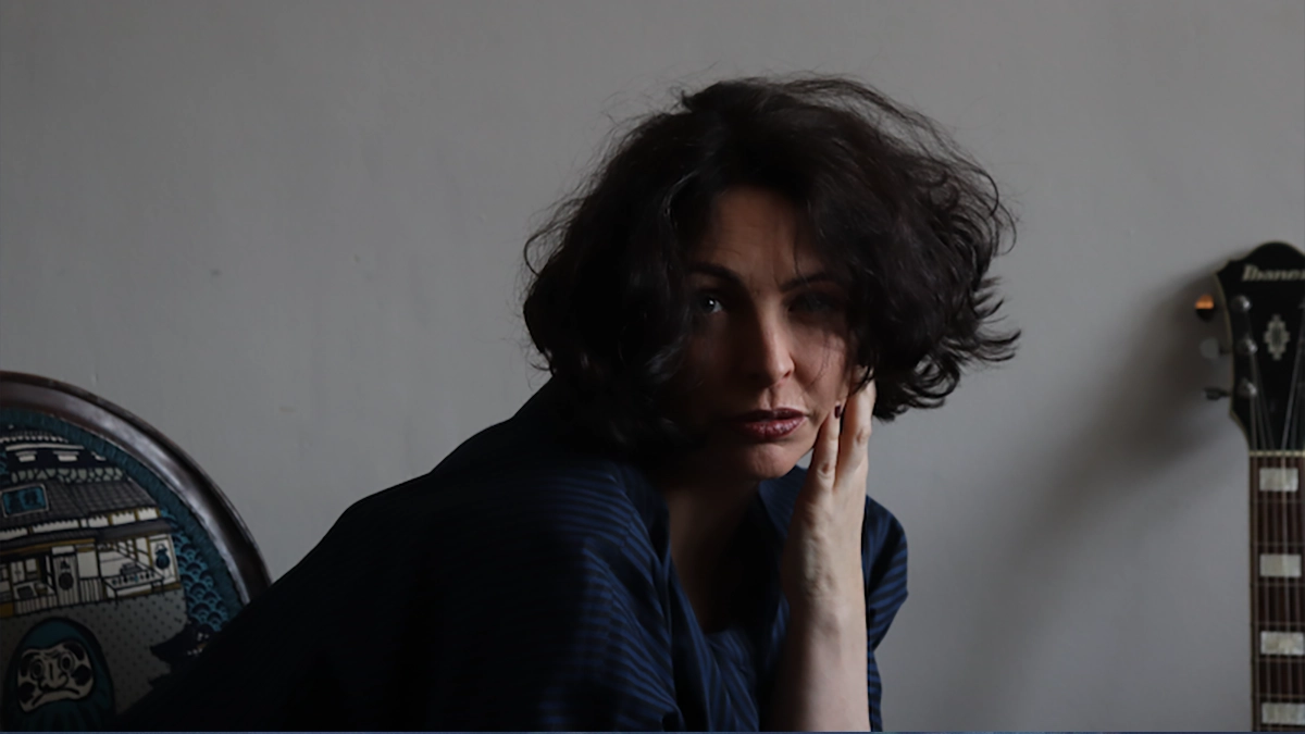 Rosalie James sat in the dim light, with only the guitar head and neck visible, the body of the guitar hidden from view beside her.