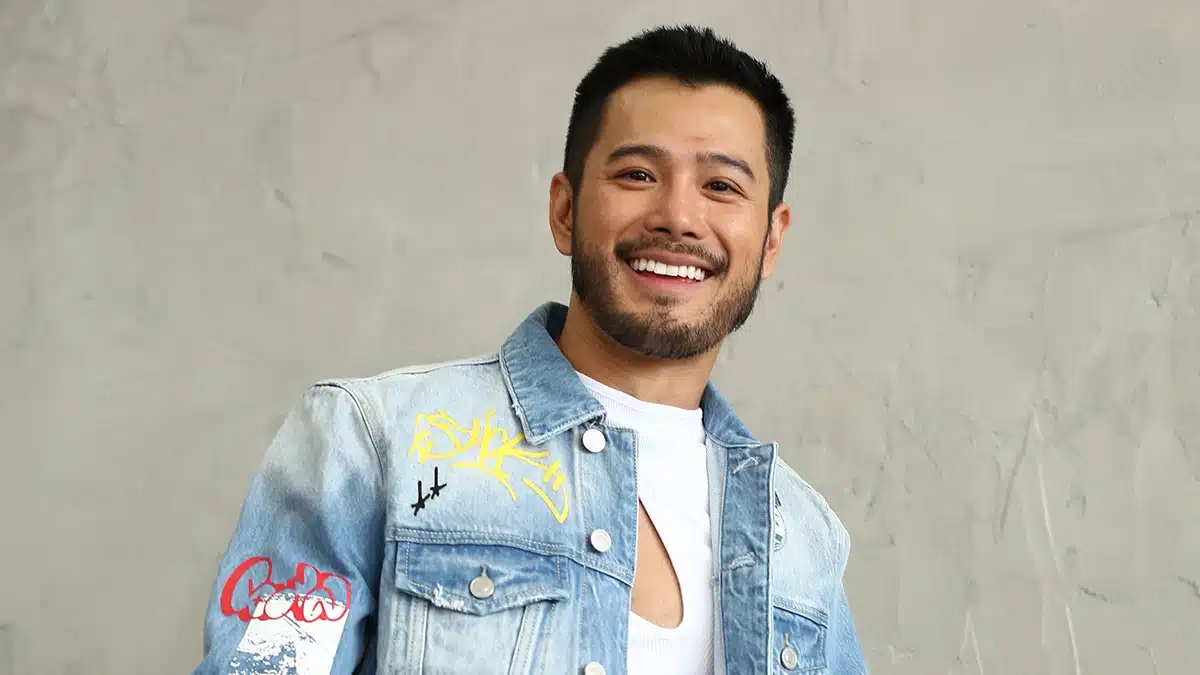 Wils in a light blue jeans jacket with a white t-shirt underneath, smiling with a beard.